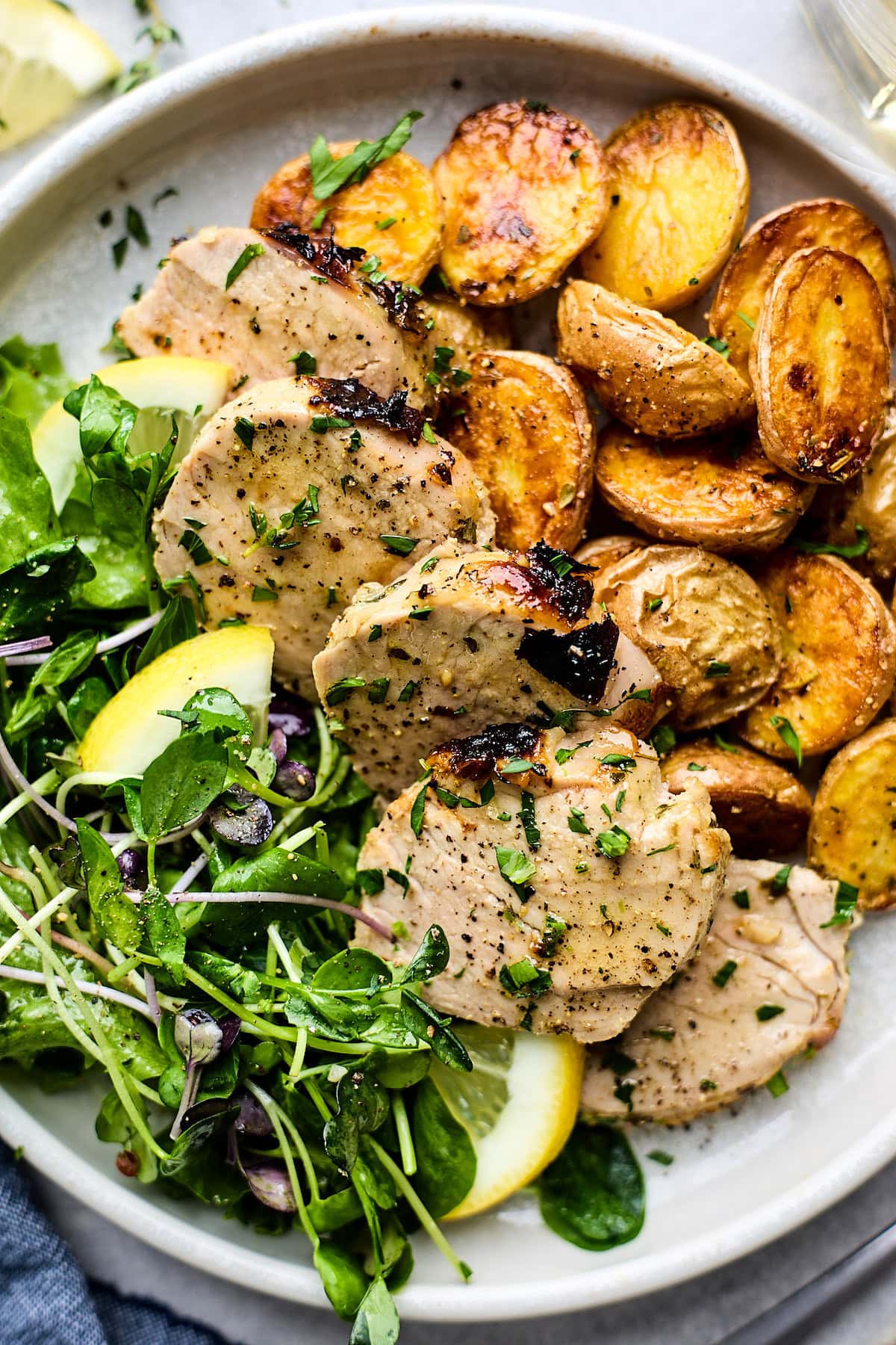 lemon herb pork tenderloin on plate with roasted potatoes and salad.