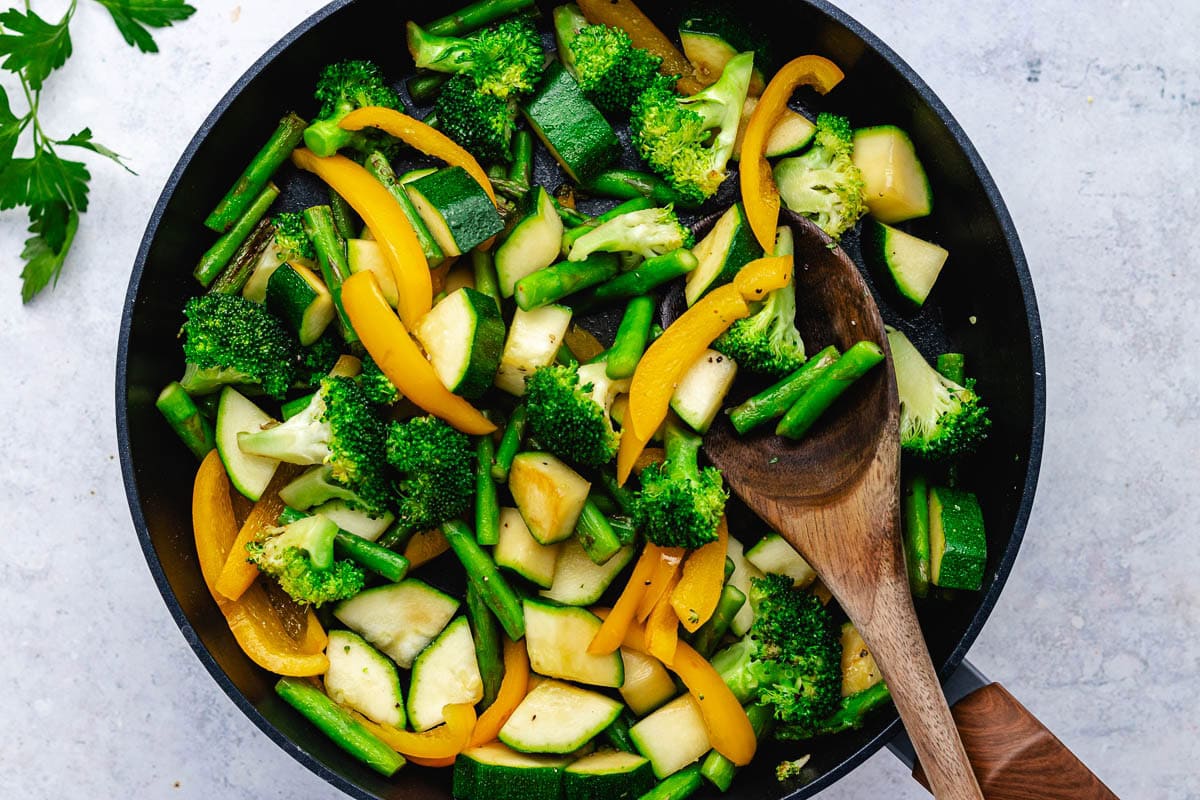 vegetables cooking in skillet with wooden spoon to make pasta primavera.
