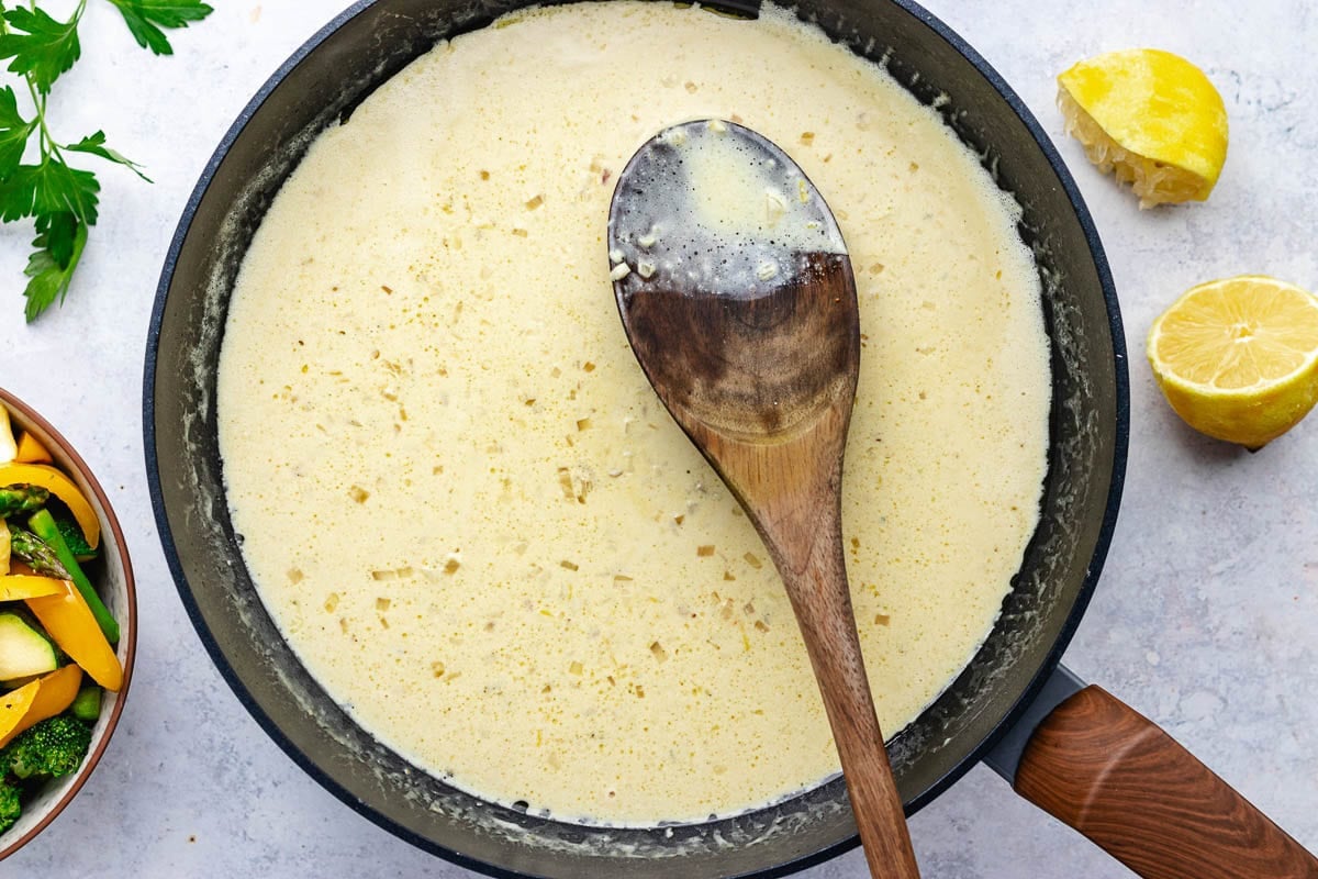 lemon cream sauce in skillet with wooden spoon to make pasta primavera.