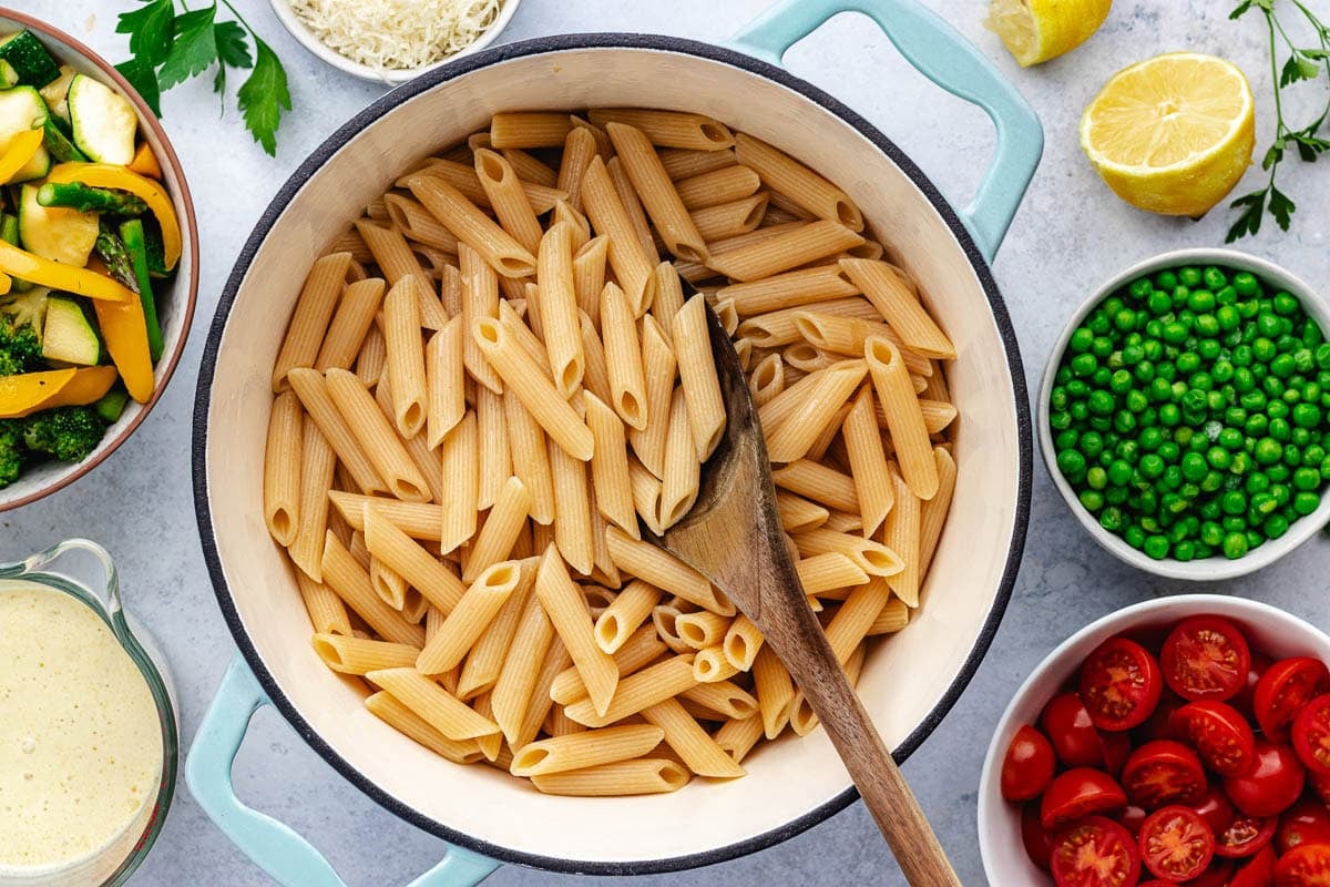 penne pasta in large pot with wooden spoon.