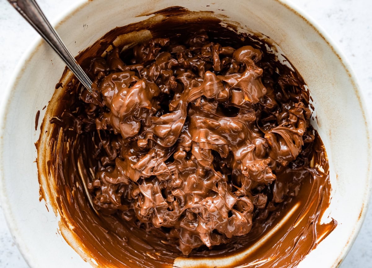 pretzels and dates being coated in melted chocolate and peanut butter in bowl.