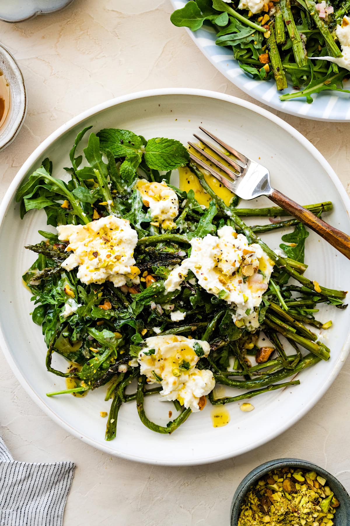 roasted asparagus with burrata, arugula, pistachios, lemon shallot dressing, and drizzle of honey on plate with fork.