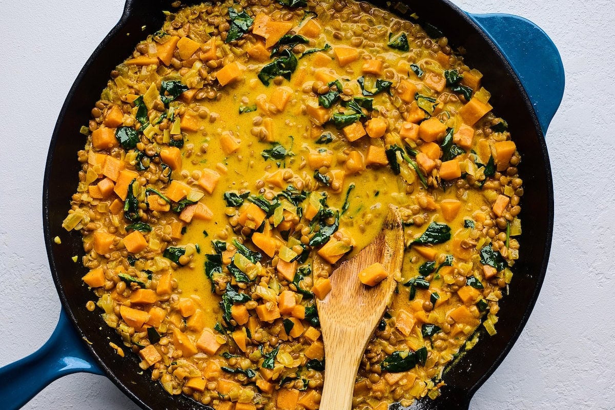 creamy sweet potatoes and lentils with spinach cooking in cast iron skillet with wooden spoon.