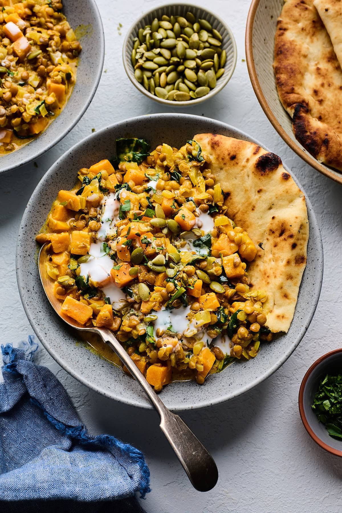 creamy sweet potatoes and lentils on plate with a drizzle of coconut milk and naan.