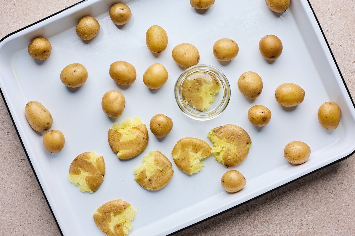 smashing baby Yukon gold potatoes with glass jar on baking sheet.