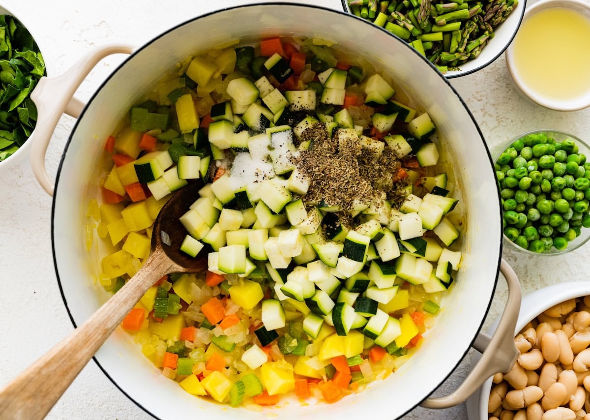 vegetables and herbs in soup pot wit wooden spoon.