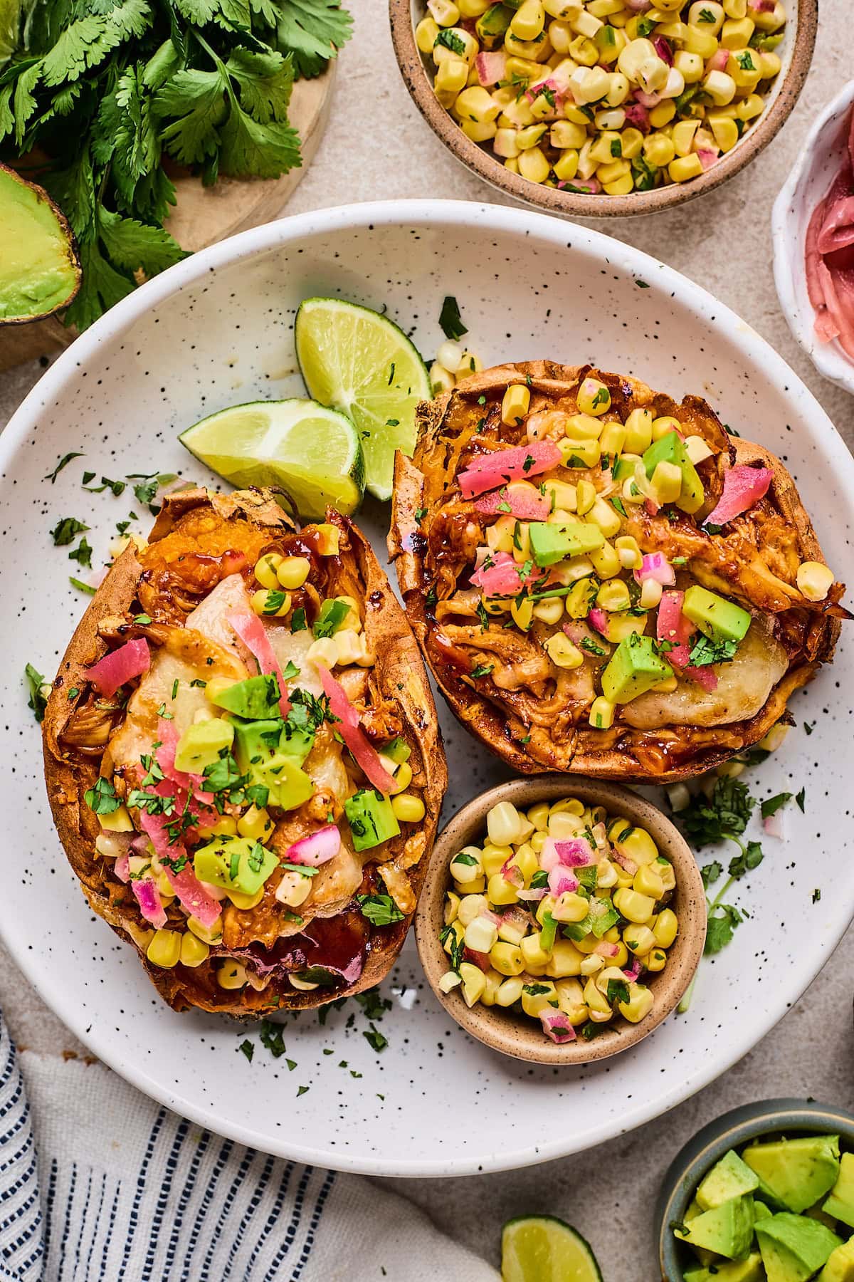 BBQ chicken stuffed sweet potatoes with corn salsa, avocado, pickled red onions, and cilantro on plate.