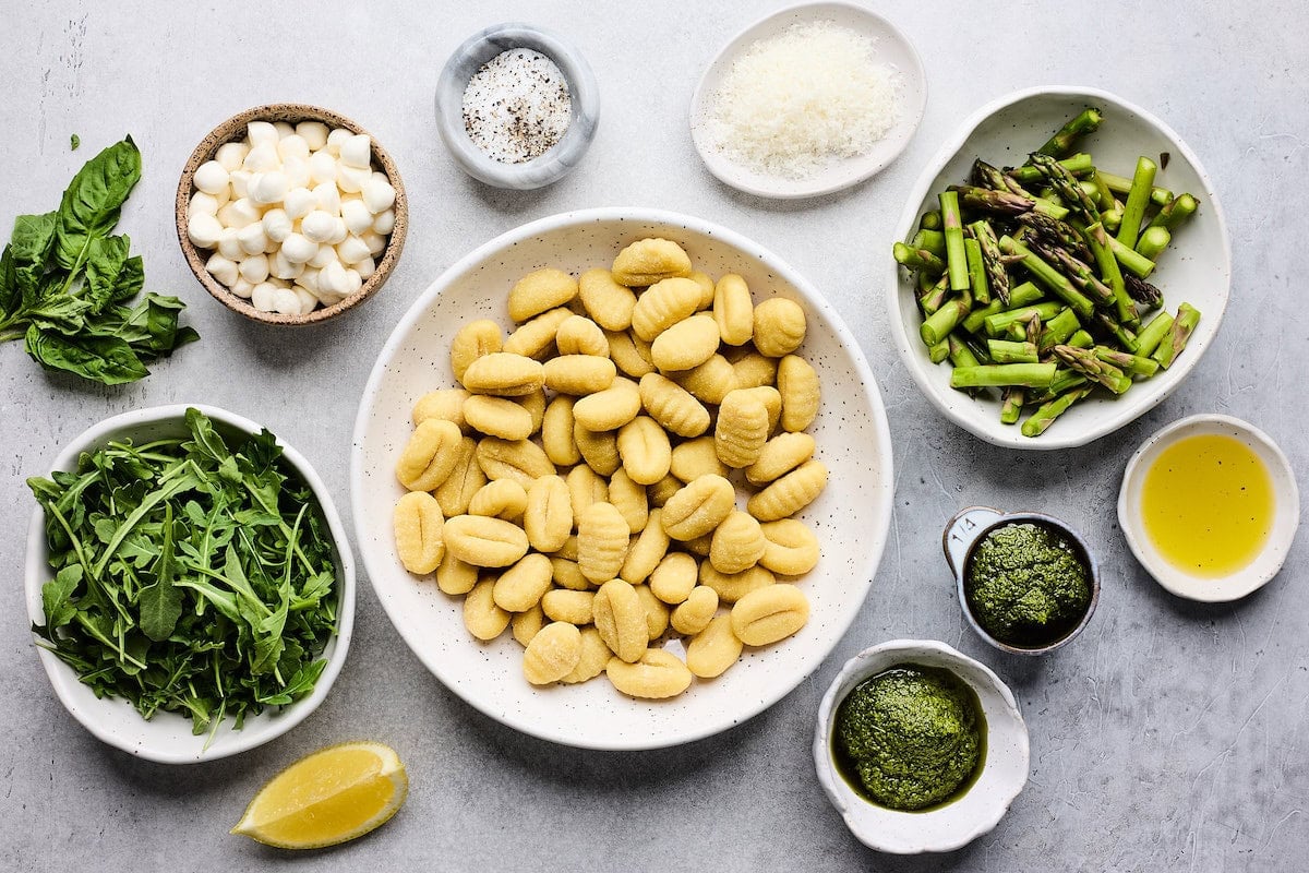 ingredients in bowls to make spring sheet pan gnocchi with pesto, asparagus, arugula, and mozzarella cheese.