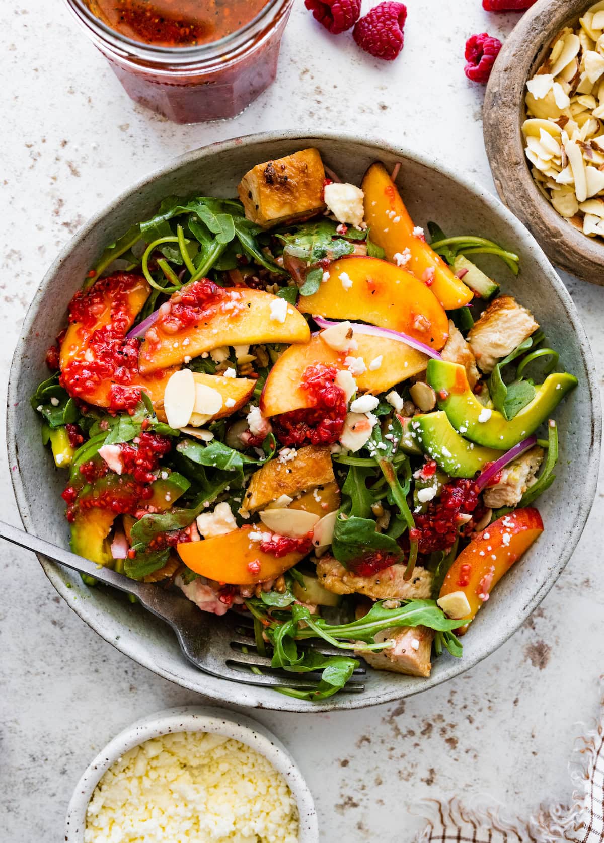 overhead shot of summer chicken salad with peaches, avocado, and fresh raspberry dressing in bowl with fork.
