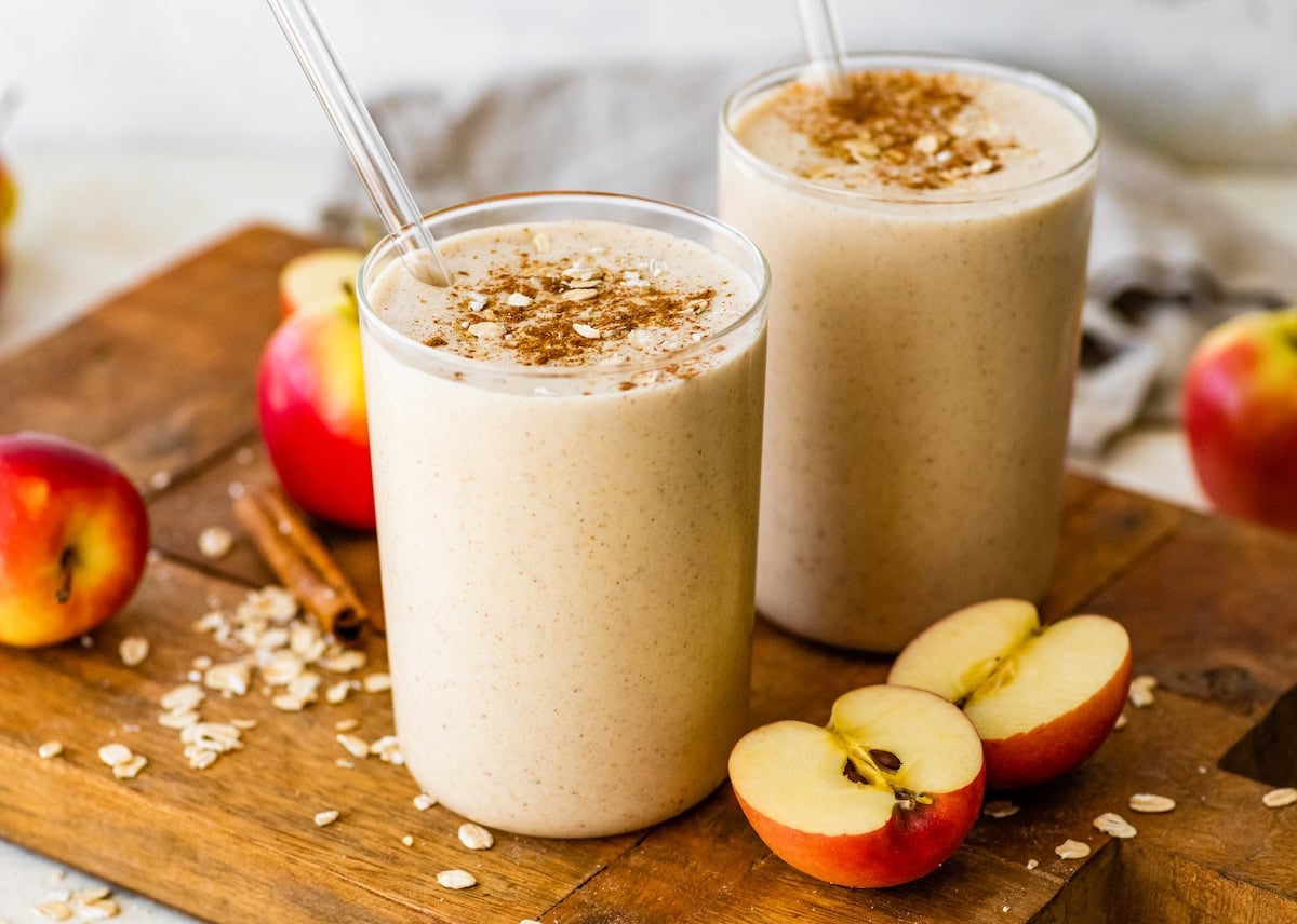 Two apple smoothies in glasses with straws topped with cinnamon and oats.