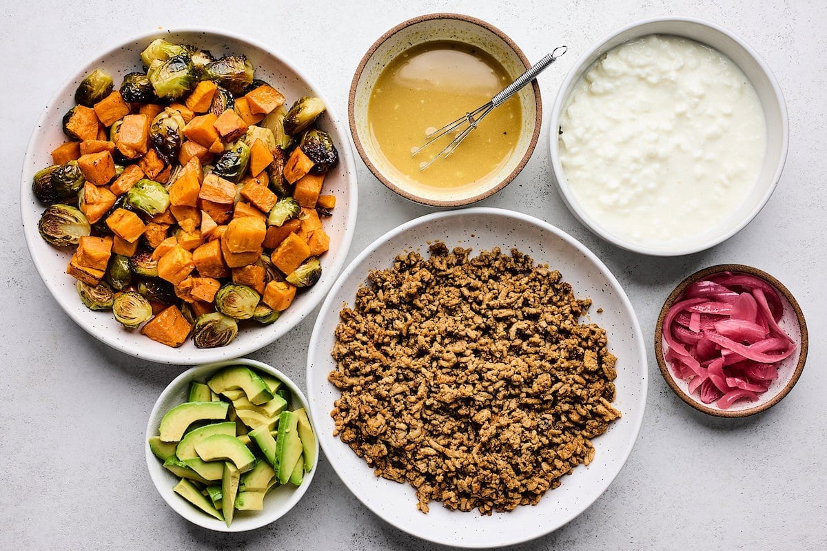 roasted veggies, cooked ground turkey, cottage cheese, avocado, pickled red onions, and maple dijon sauce in bowls to make ground turkey bowls.