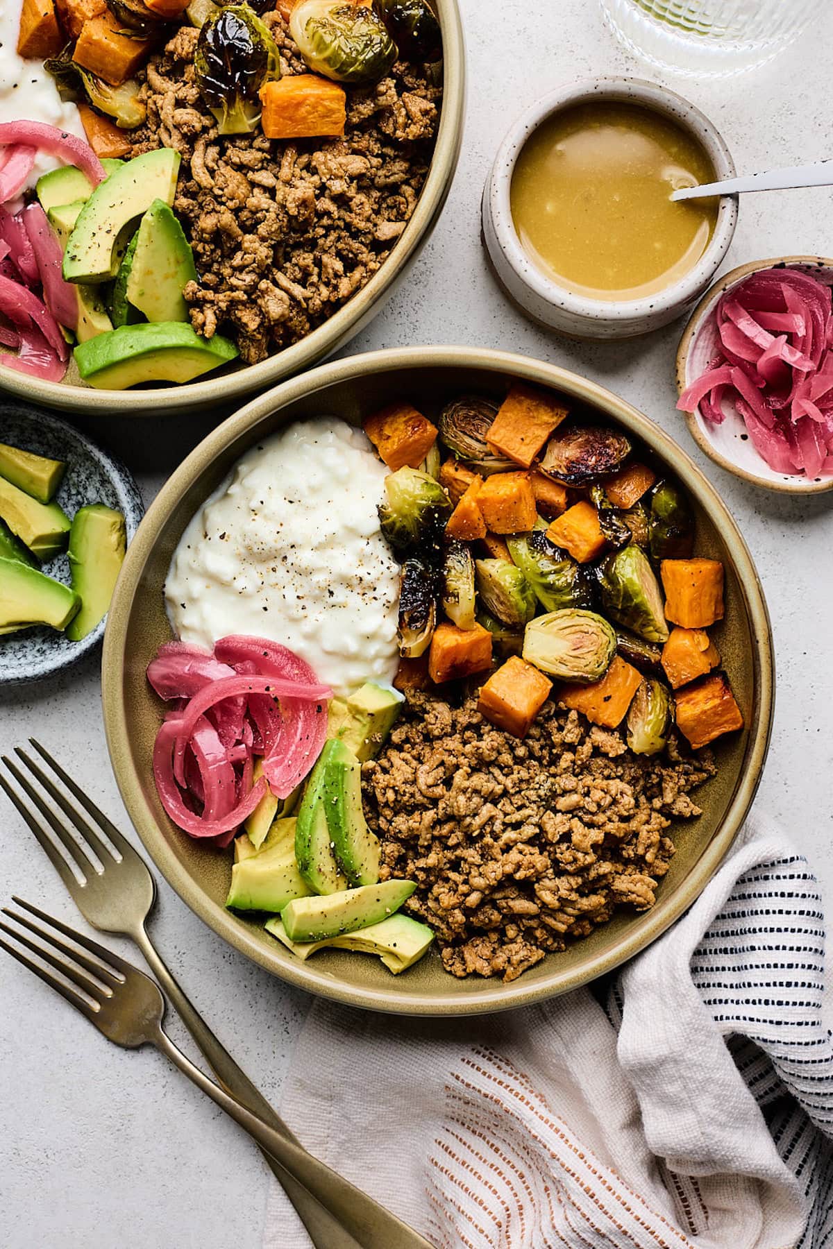 ground turkey bowl with roasted vegetables, cottage cheese, avocado, and pickled red onions with maple dijon sauce in a small bowl.