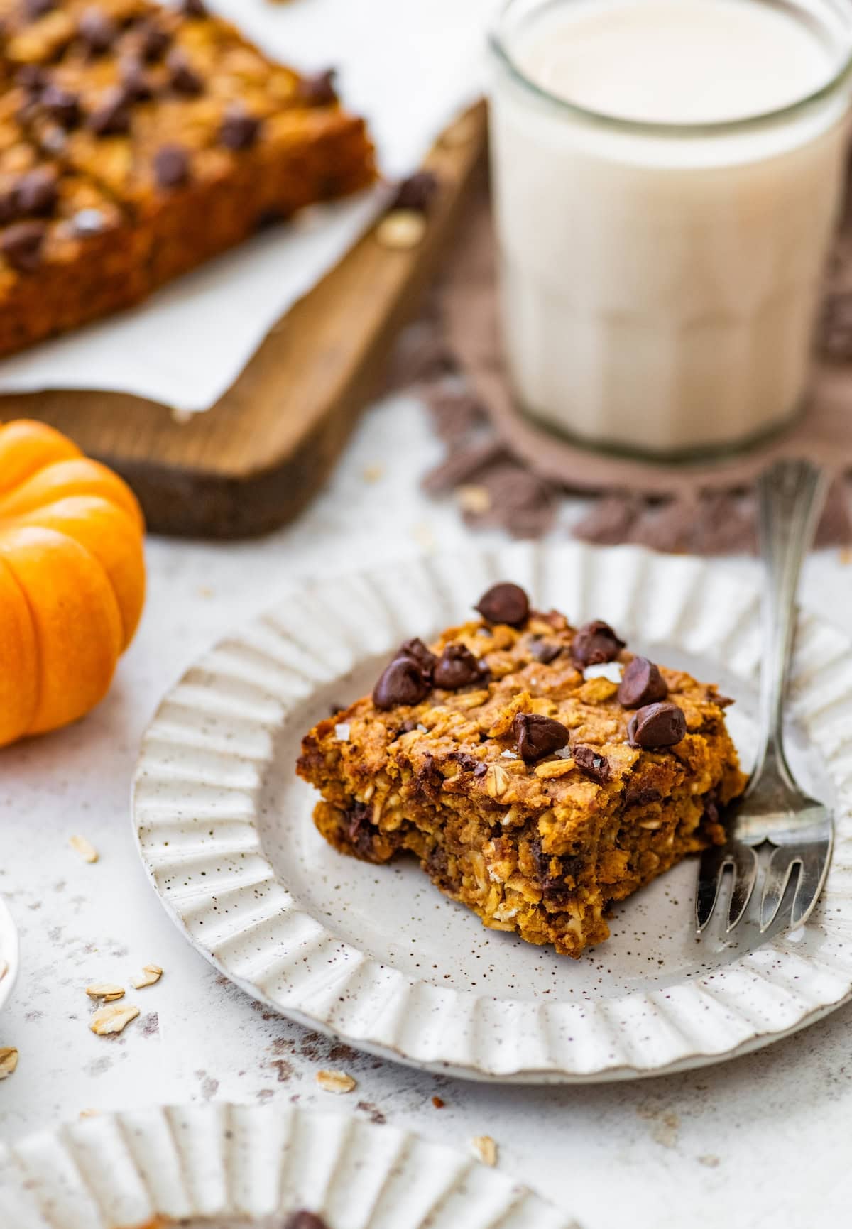 piece of pumpkin chocolate chip oatmeal bar on plate with fork and glass of milk.