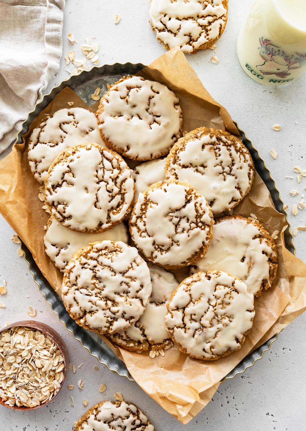 eggnog iced oatmeal cookies on tray with parchment paper and glass of eggnog.