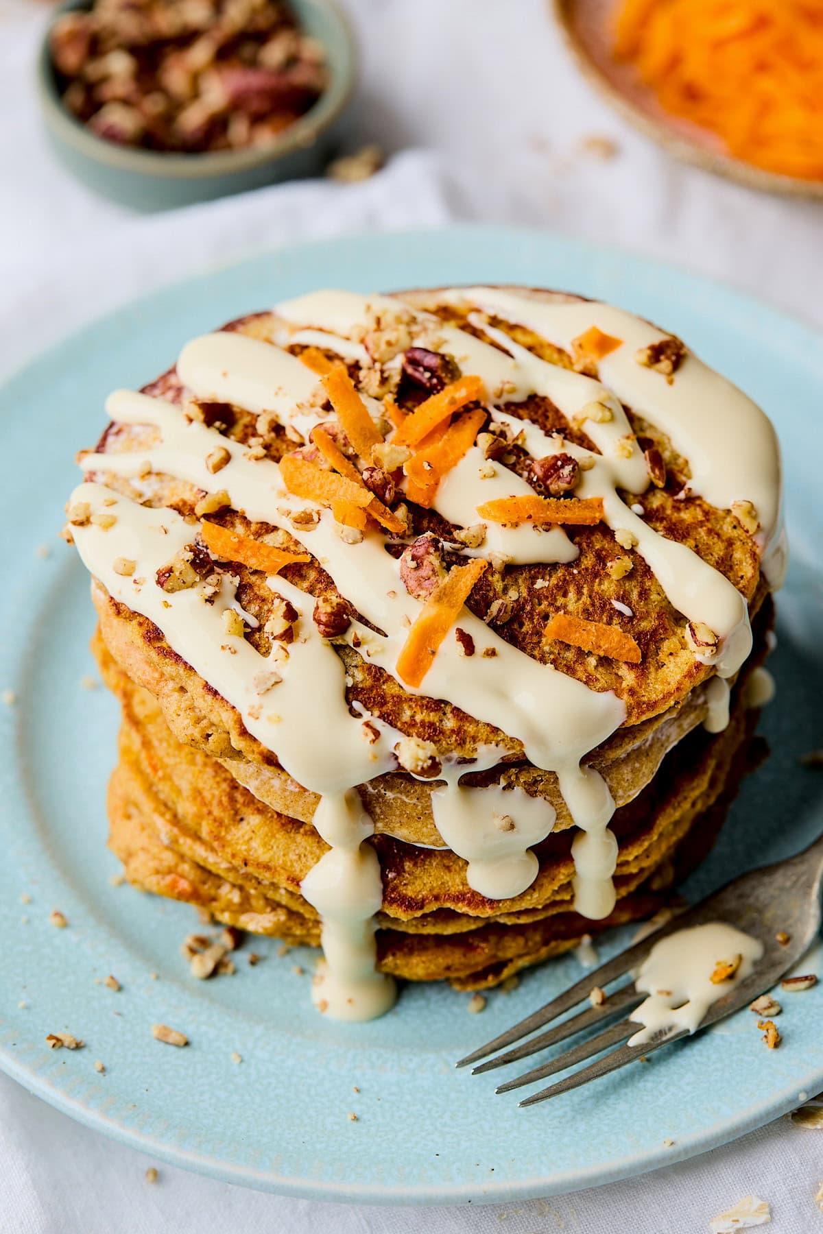 stack of carrot cake pancakes with maple cream cheese glaze on plate with fork.